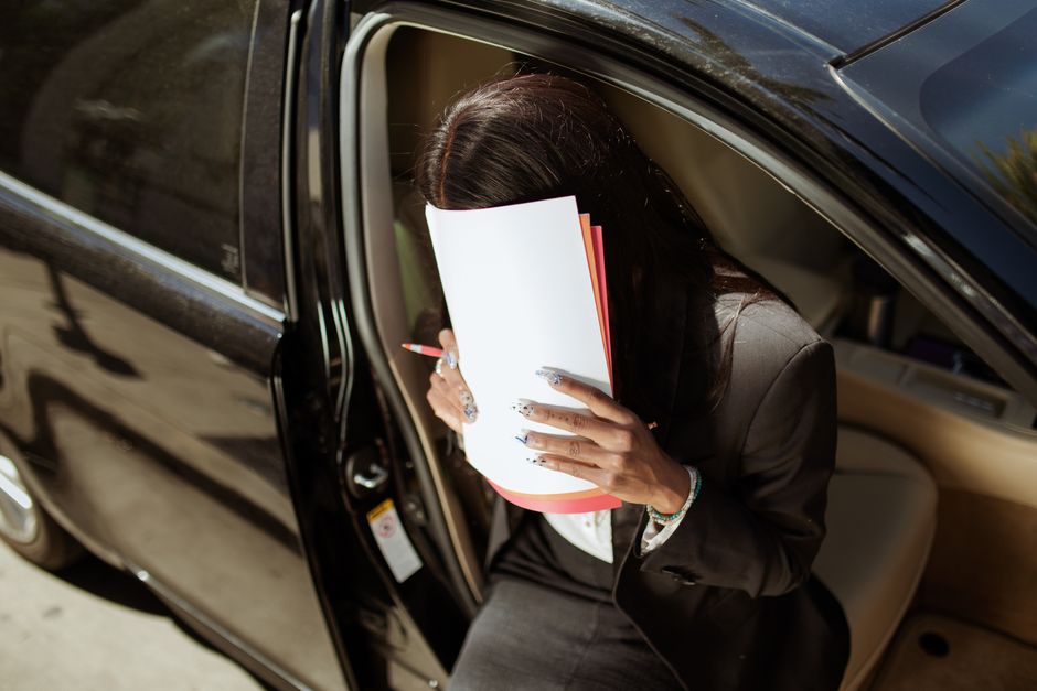 A businesswoman sits in a car reviewing documents on a sunny day.