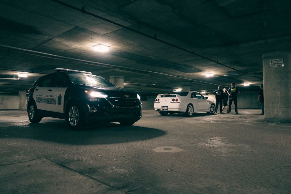 Police vehicles and a group of people in an underground parking lot. Dramatic lighting sets the scene.